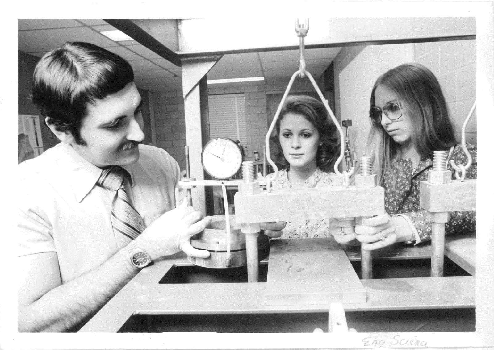 A vintage photo of a professor and two students working with a piece of equipment