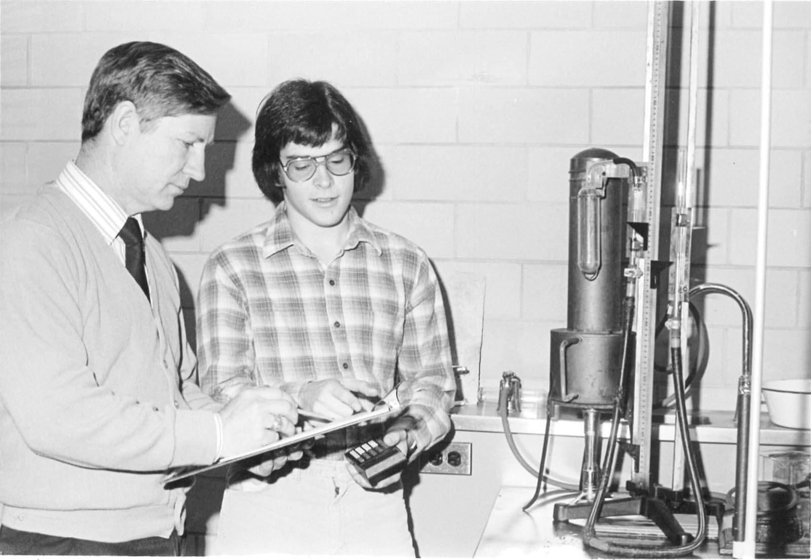 A vintage photo of a researcher and a student working with a piece of equipment