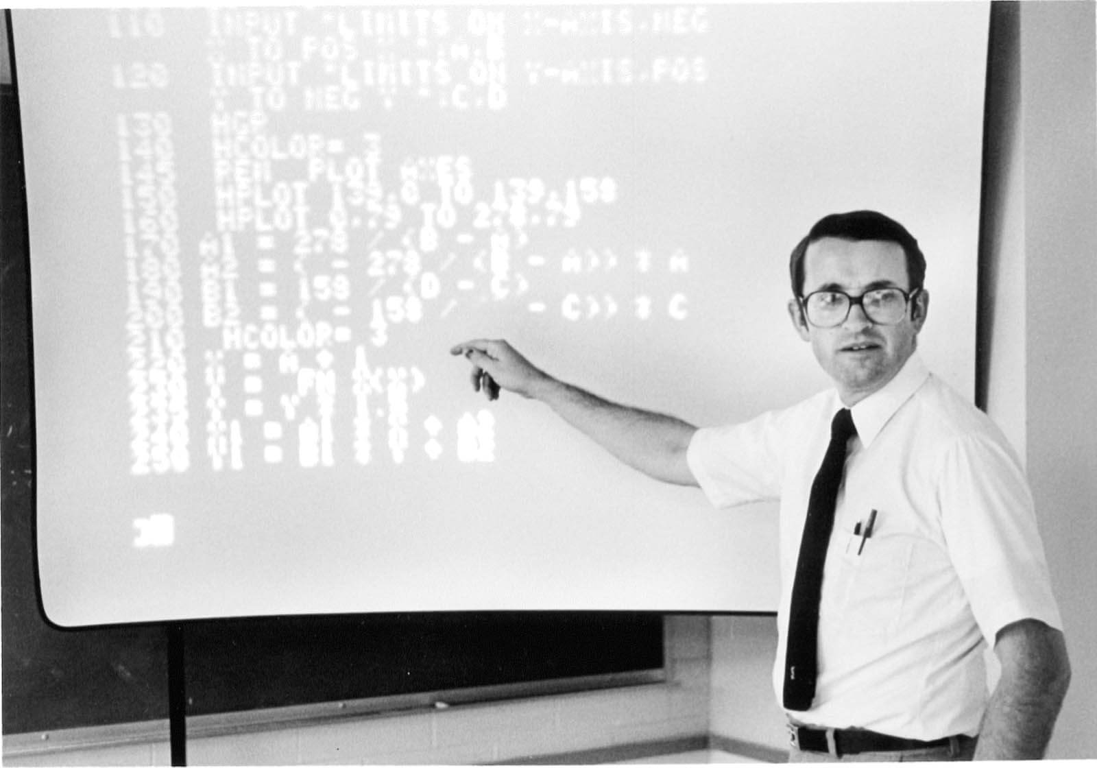 A vintage photo of a professor pointing at projection of data on a wall